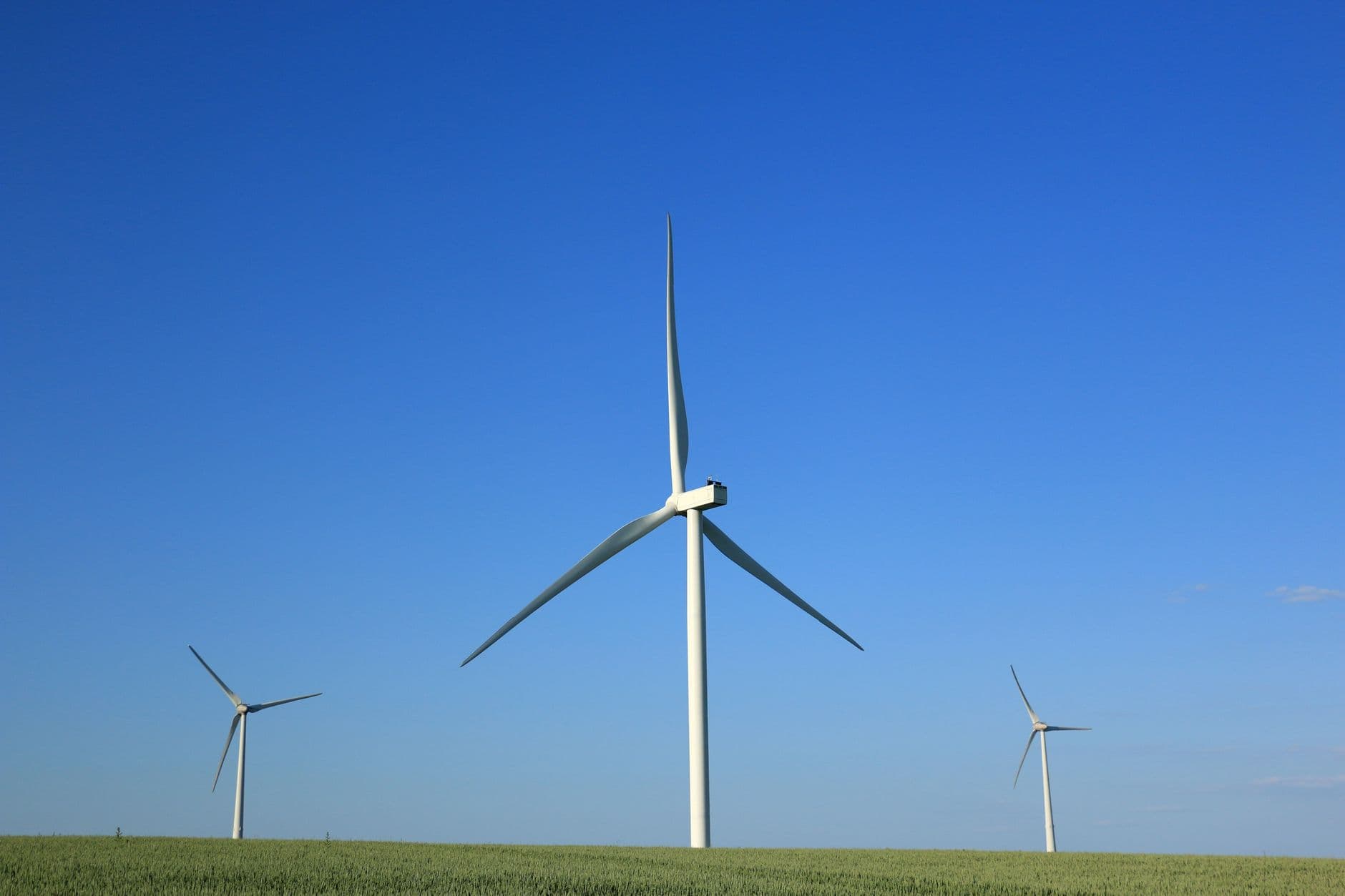 Drie windturbines in een vlak groen akkerveld onder een strakblauwe lucht