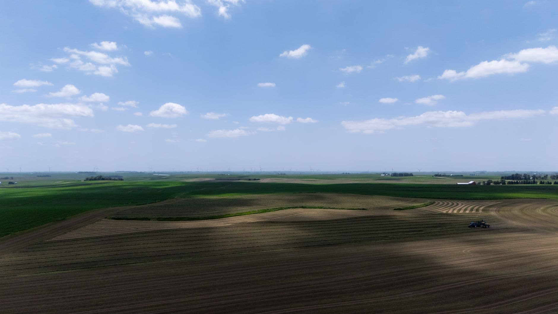 Vlakke akkers tot aan de horizon met een tractor in de verte en windturbines aan de einder
