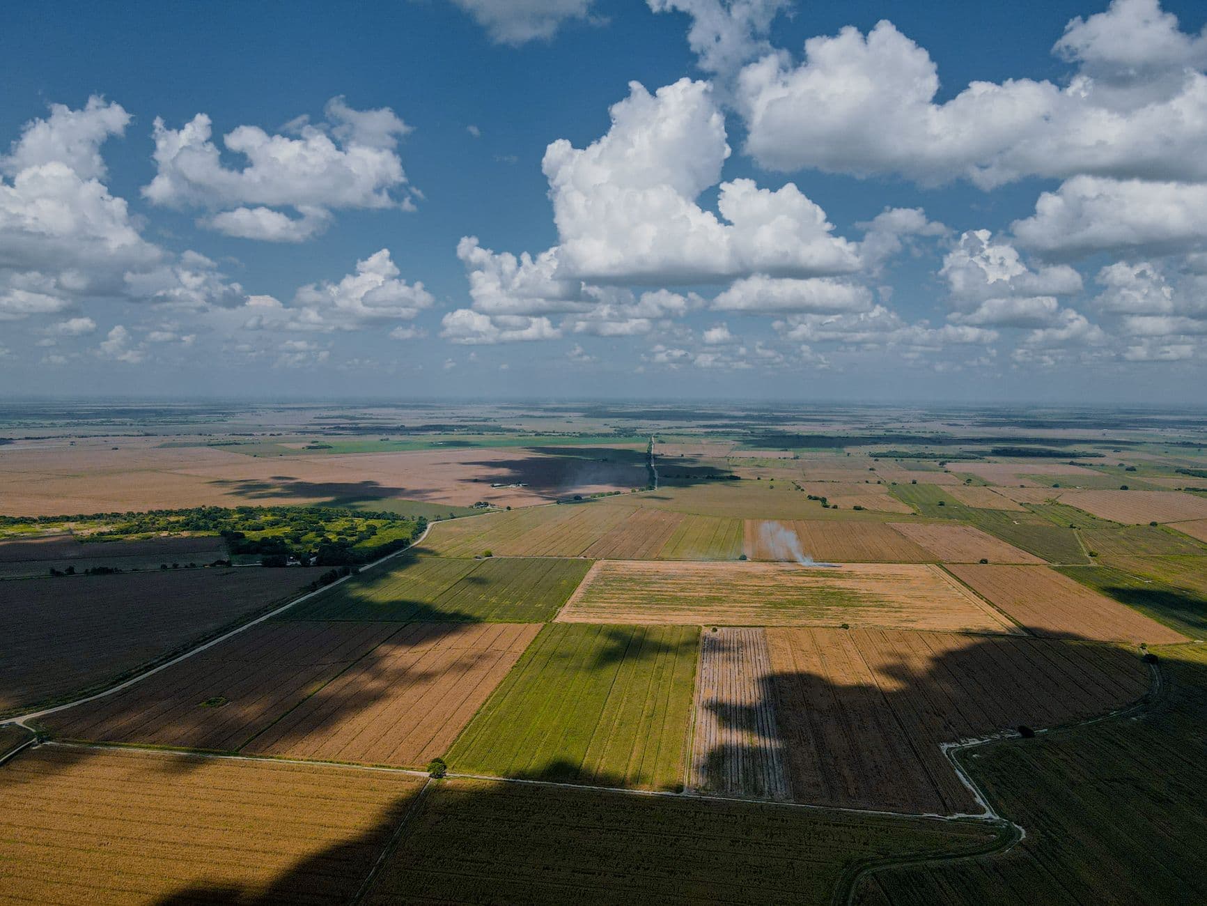 Vlakke akkers en weilanden van bovenaf gezien onder een blauwe lucht met stapelwolken