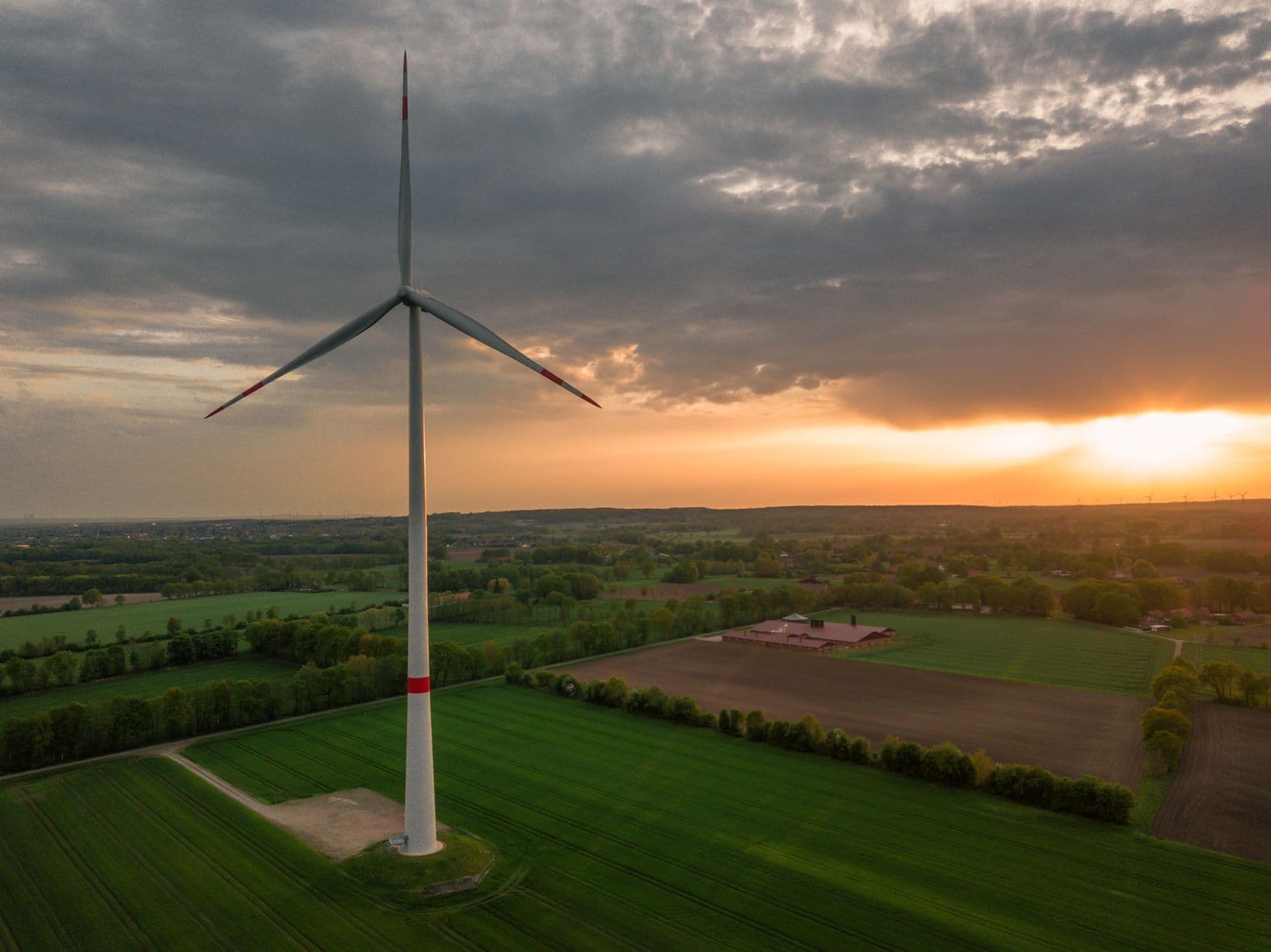 Windturbine boven groene akkers en bomenrijen bij zonsondergang