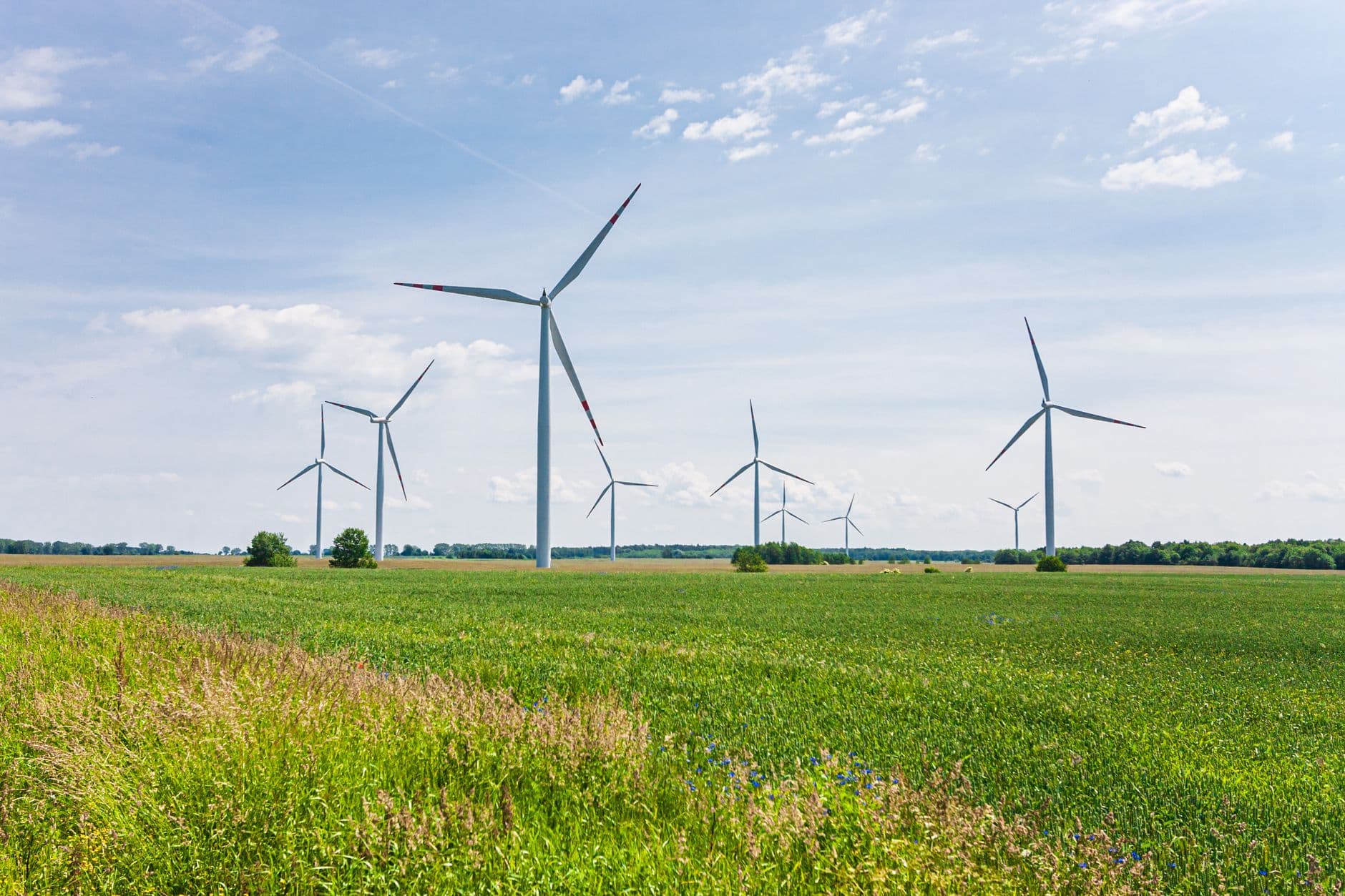 Rij windturbines in een vlak groen veld onder een lichtblauwe lucht met wolken