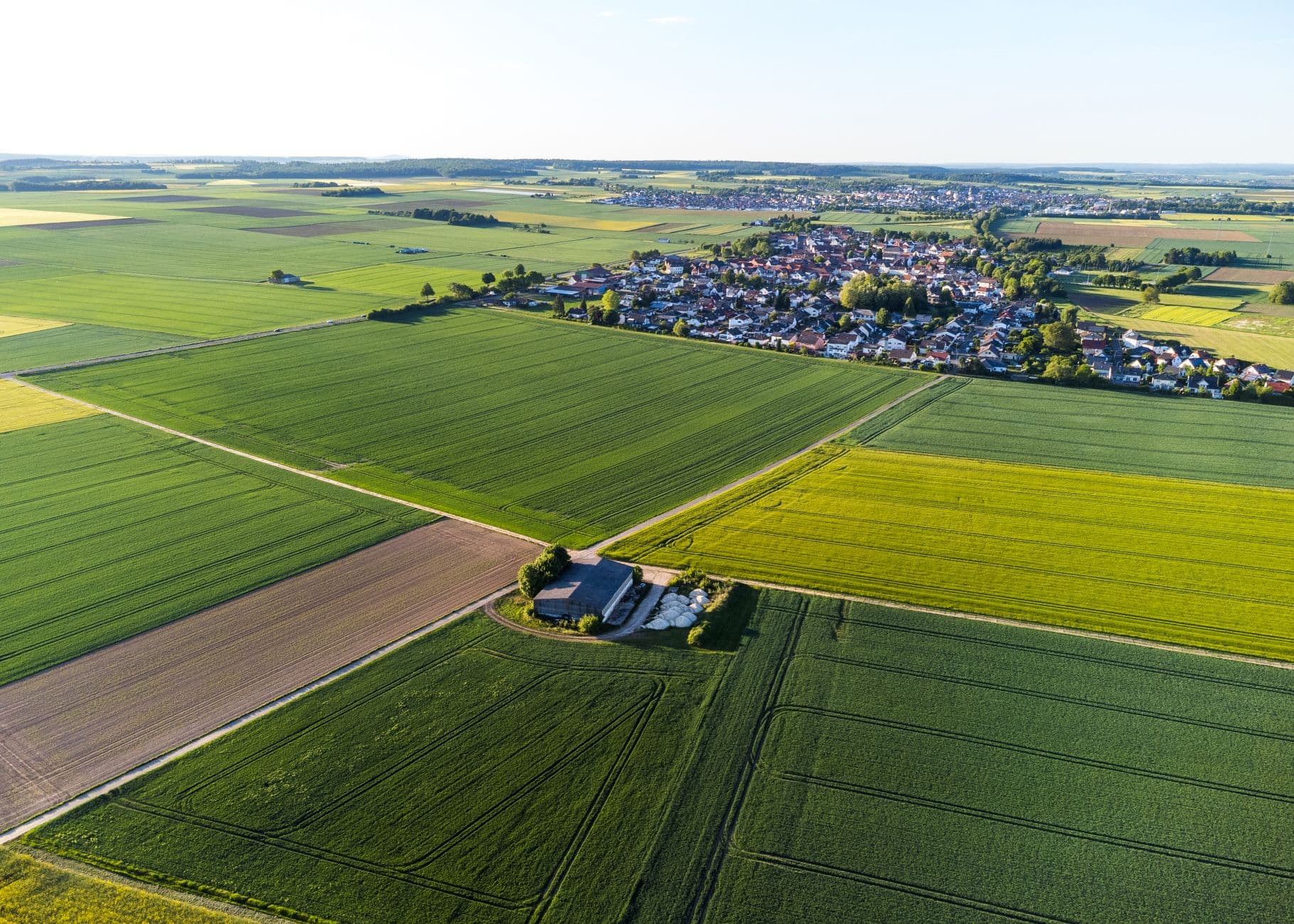 Groene akkers en een koolzaadveld met daarachter een dorp met rode daken, van bovenaf gezien