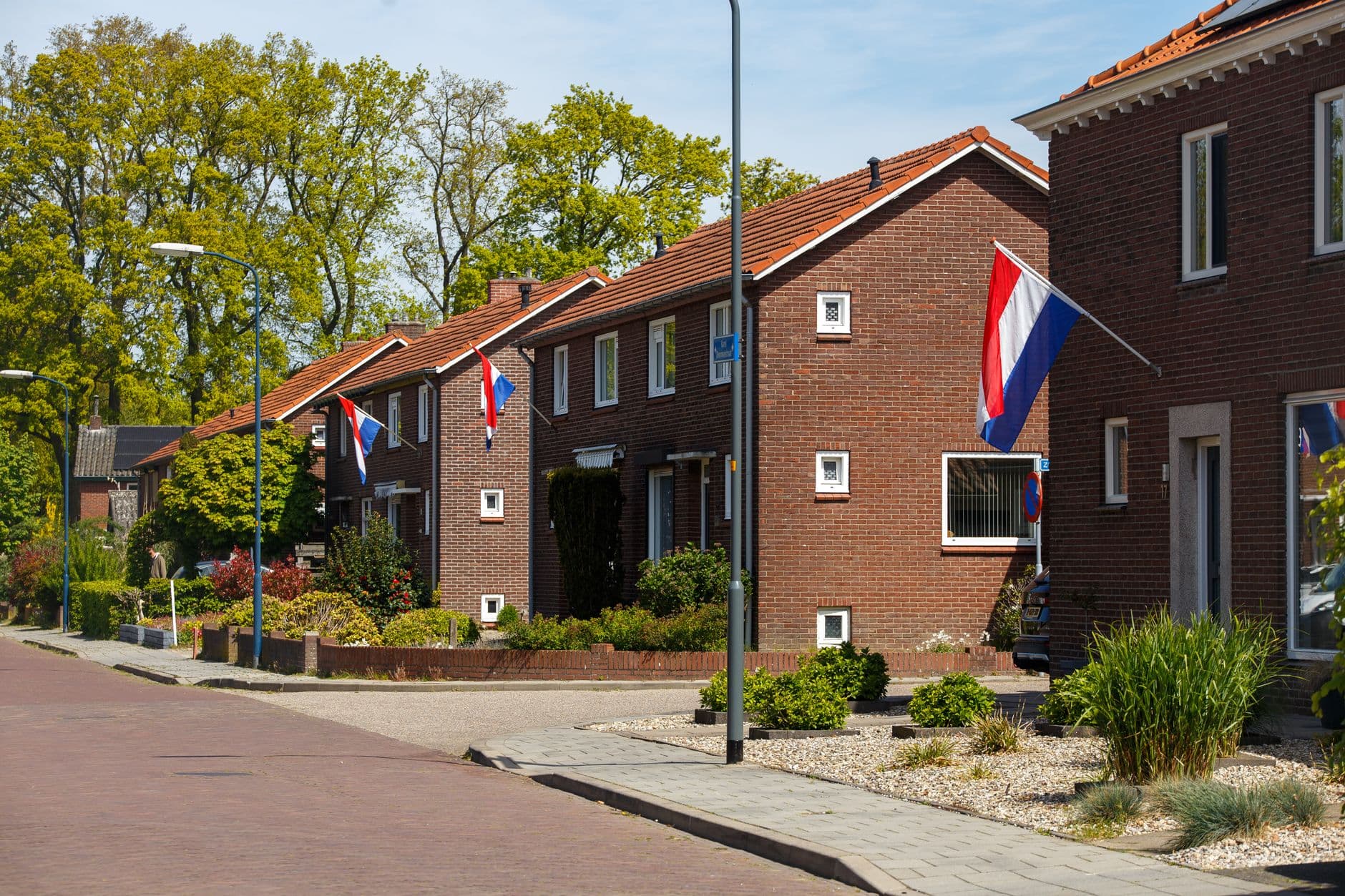 Woonstraat met bakstenen woningen en Nederlandse vlaggen op een zonnige dag