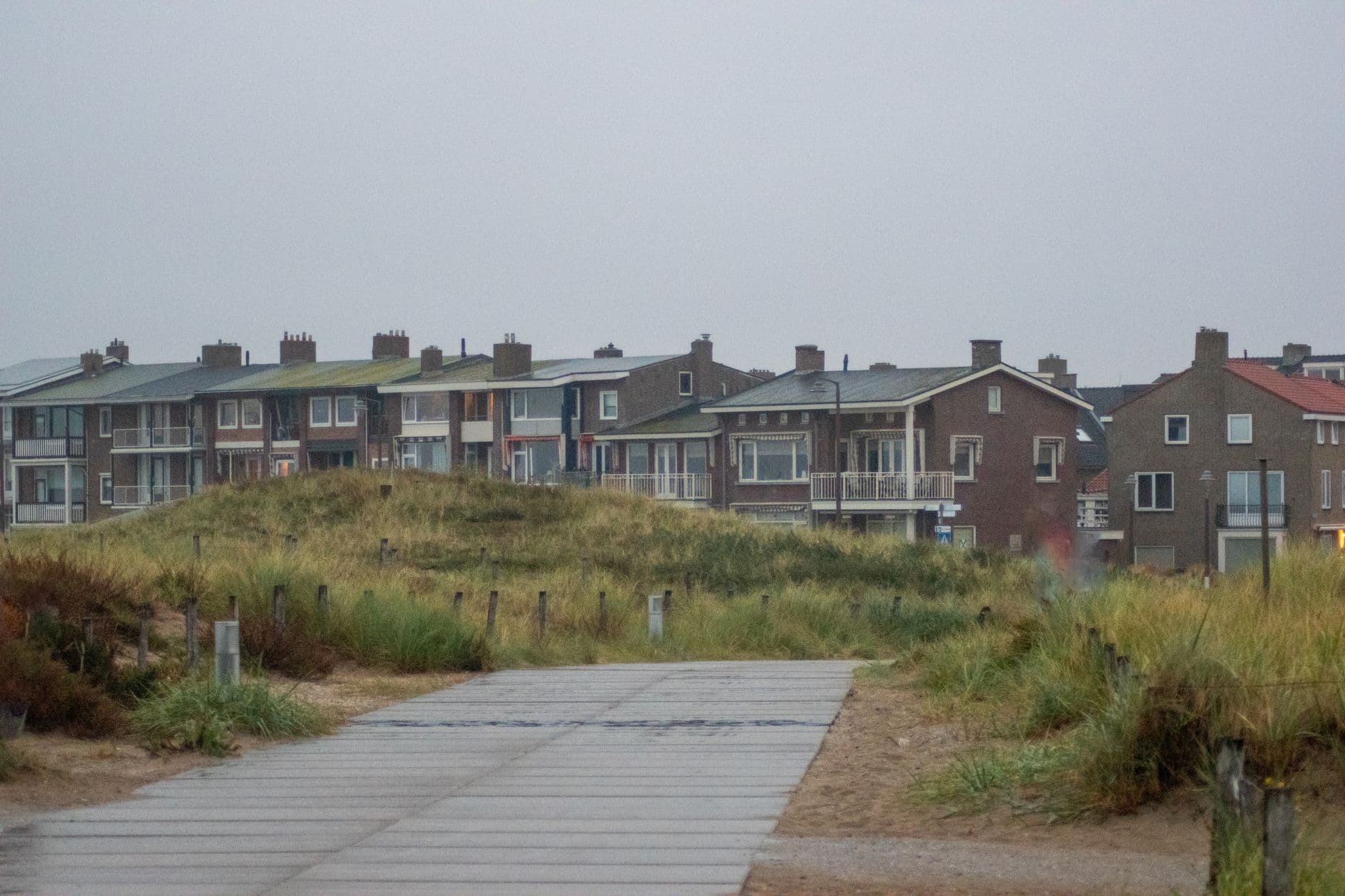 Woningen en appartementen met balkons achter de duinen, met een houten pad op de voorgrond