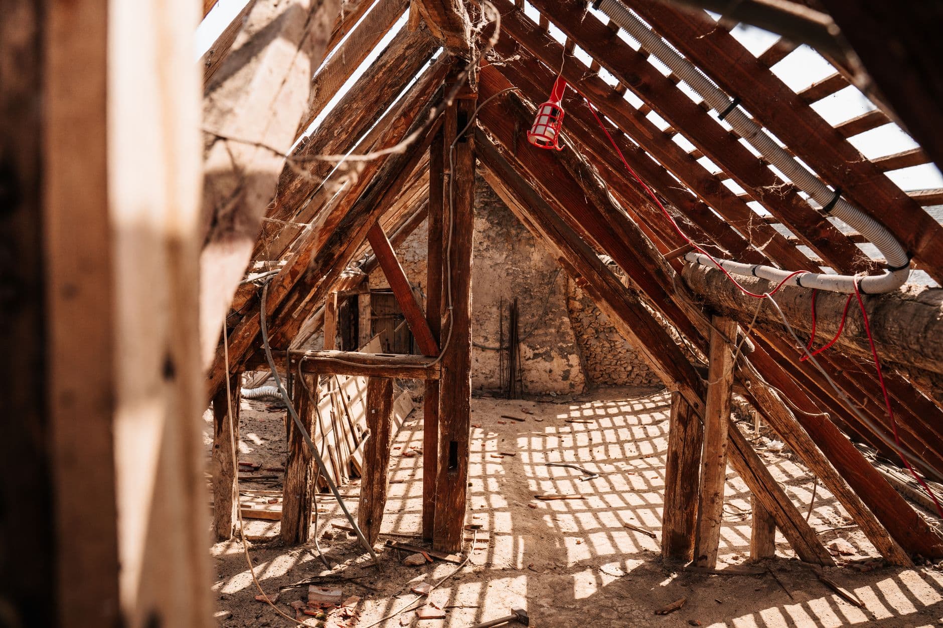 Onafgewerkte zolder met oude houten dakspanten zonder isolatie, zonlicht valt door kieren in het dak